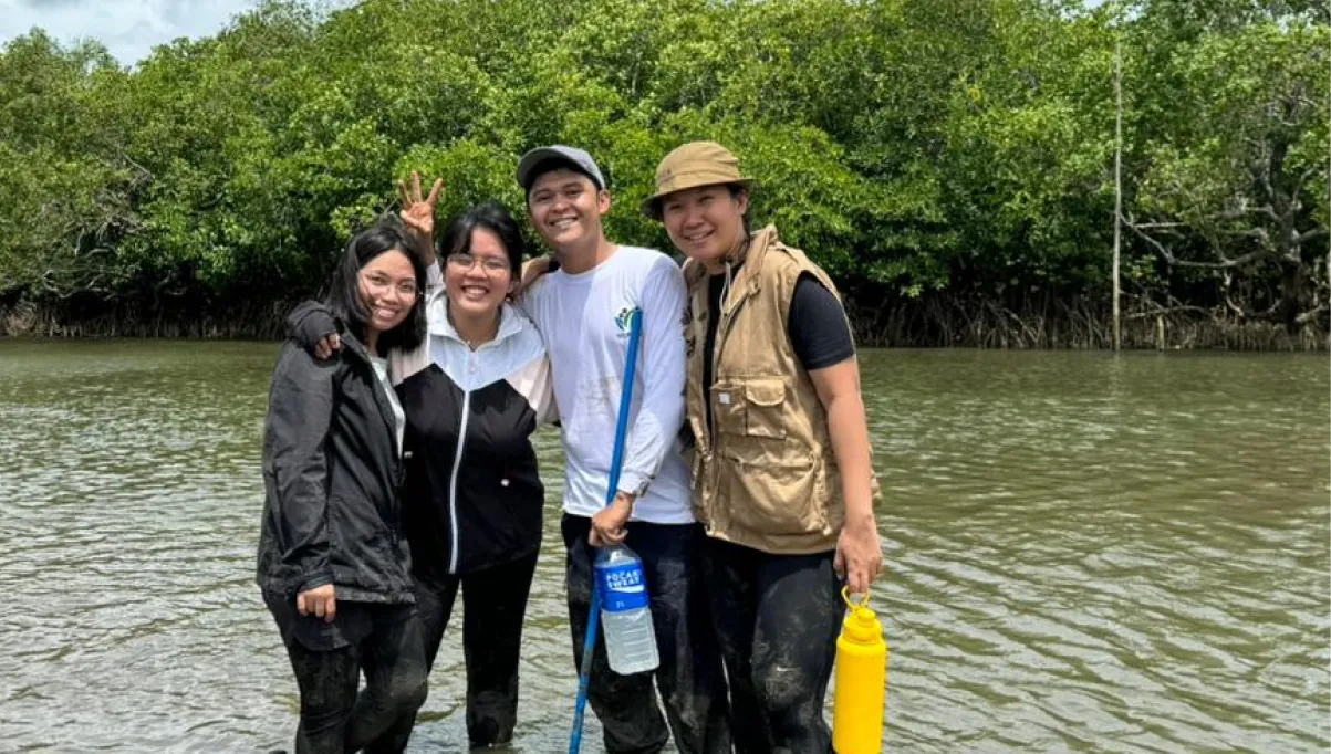 Four people standing in shallow water with green mangrove trees in the background, smiling and posing.
