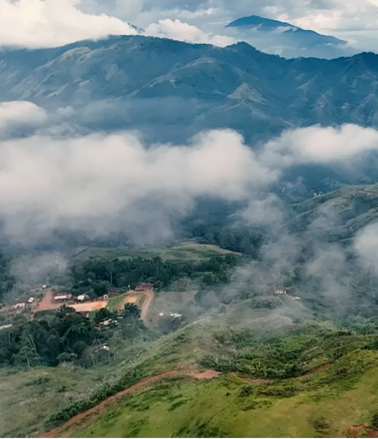 Clouds drifting over green hills and forested mountains under a partly cloudy sky.